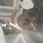 Machining process in action with a metal component being cut or shaped, coolant spray visible, partially obscuring the view.