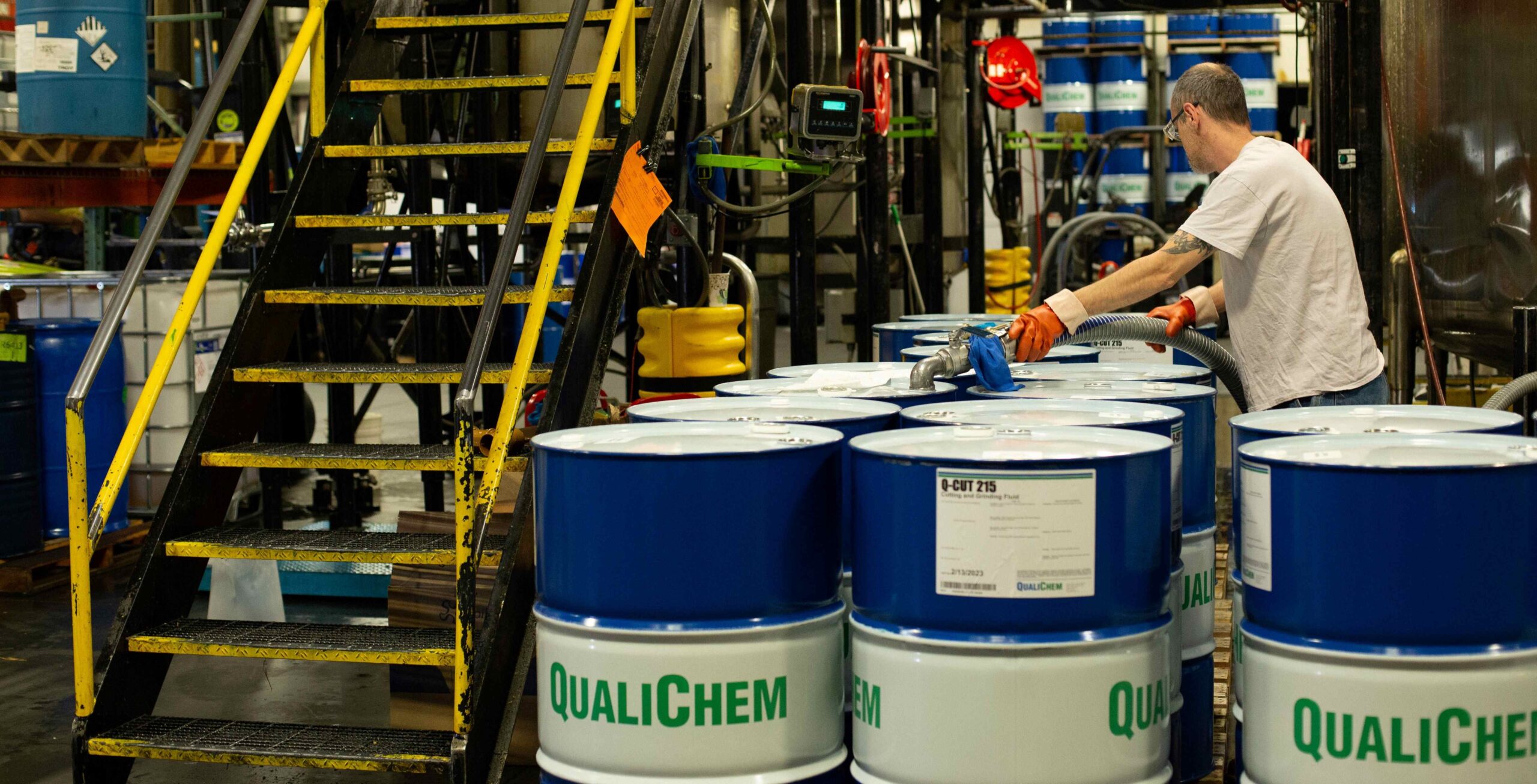 A worker in a warehouse is handling chemical drums labeled 