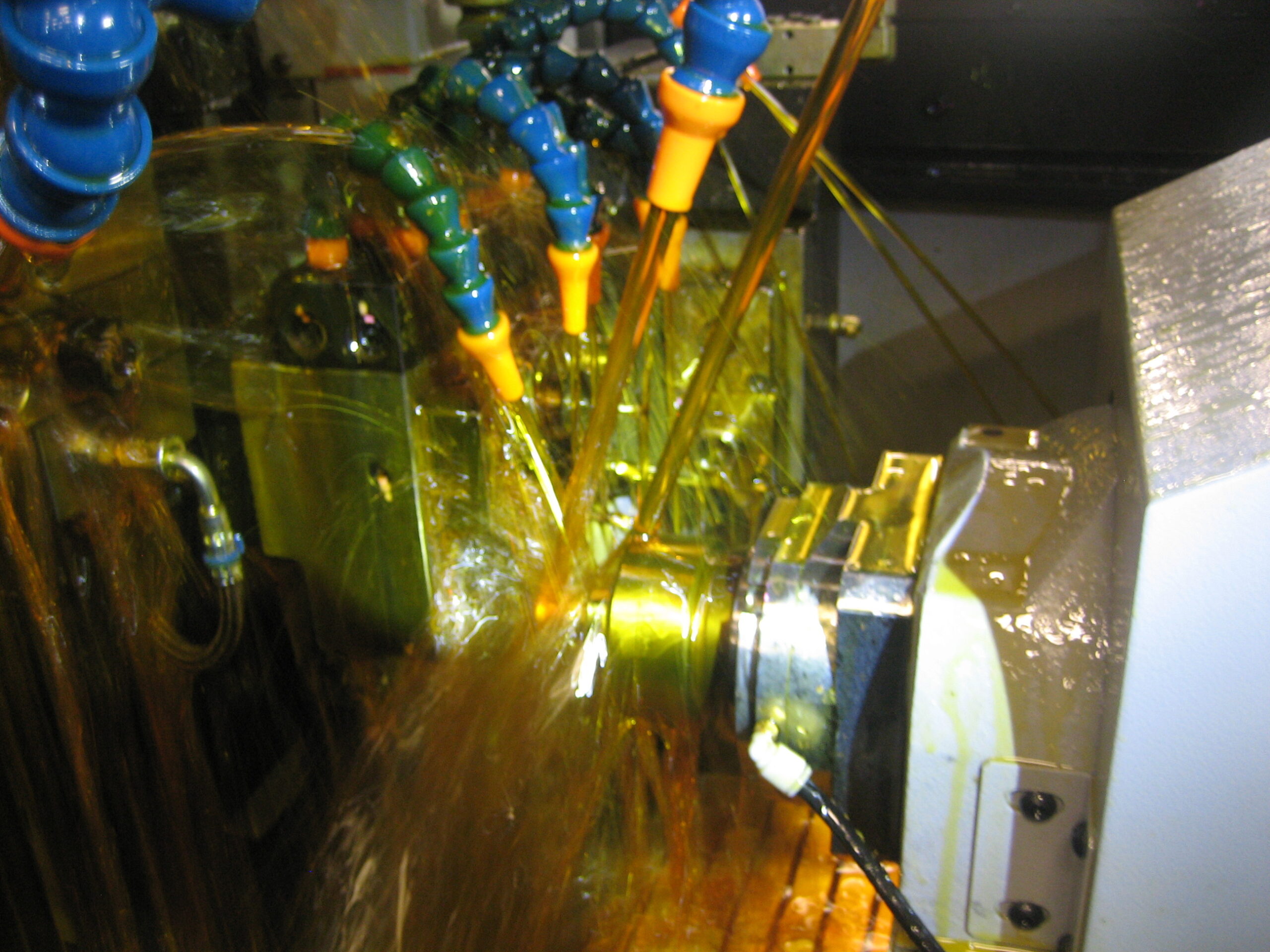 A dynamic industrial scene showing a metal component being cooled with a spray of liquid from multiple nozzles during a machining process.