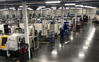 Wide-angle view of a large industrial manufacturing floor filled with various machinery and few workers in the distance.